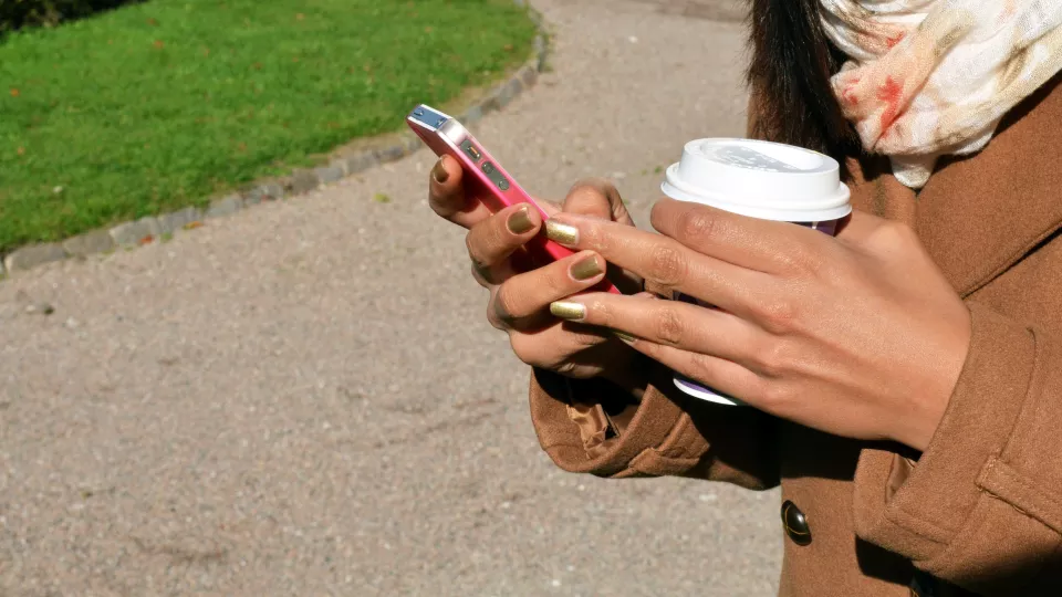 Hand som håller en iphone och en kaffekopp