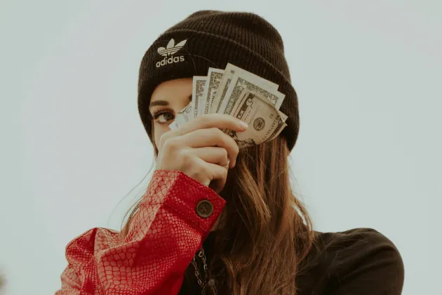 Ung person som håller sedlar för ansiktet. Foto: Joshua Rondeau, Unsplash.