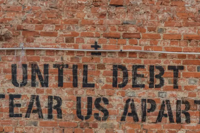 Tegelvägg med texten: Until debt tear us apart.
