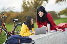 Foto. Två studenter utomhus tittar på dator. I bakgrunden en cykel. Fotograf: Johan Persson