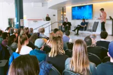 Publik tittar på en scen där tre personer pratar. Foto.